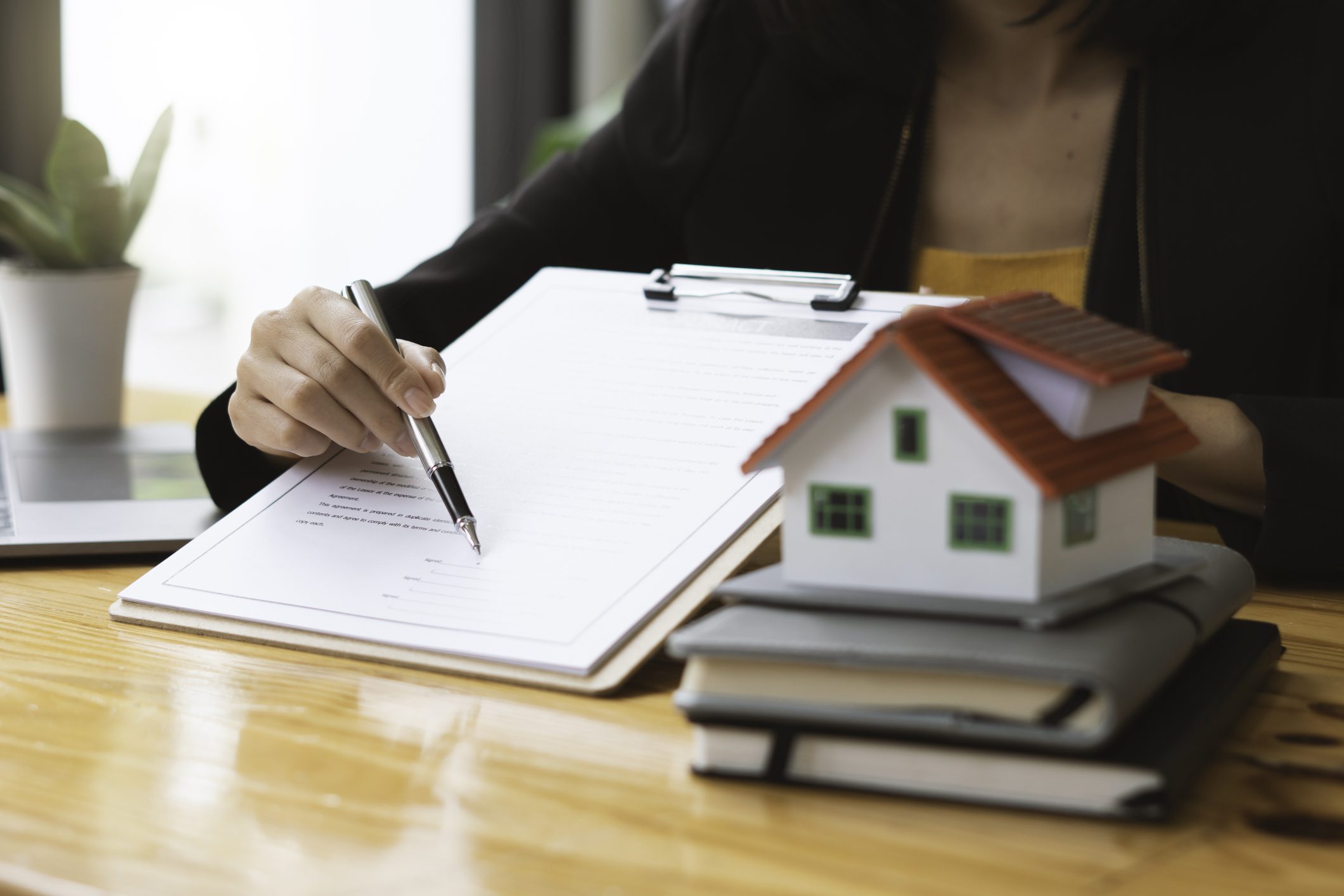 Person signing documents beside a model house.