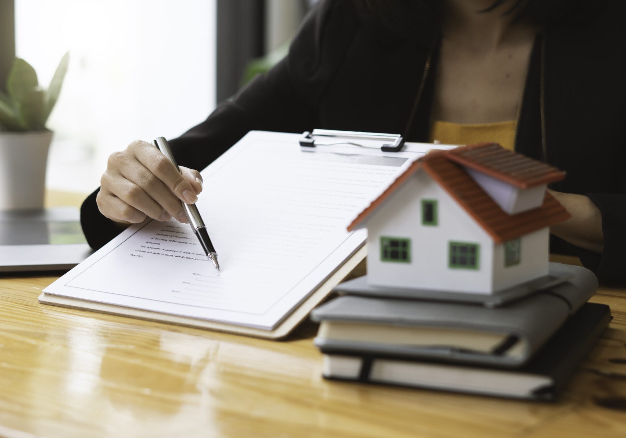 Person signing documents beside a model house.